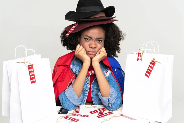 Black young woman frowning while posing with shopping bags isolated over white background