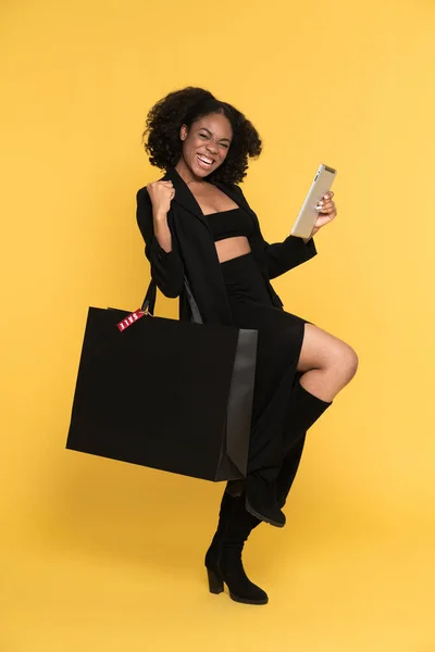 Black woman using tablet computer while making winner gesture isolated over yellow background
