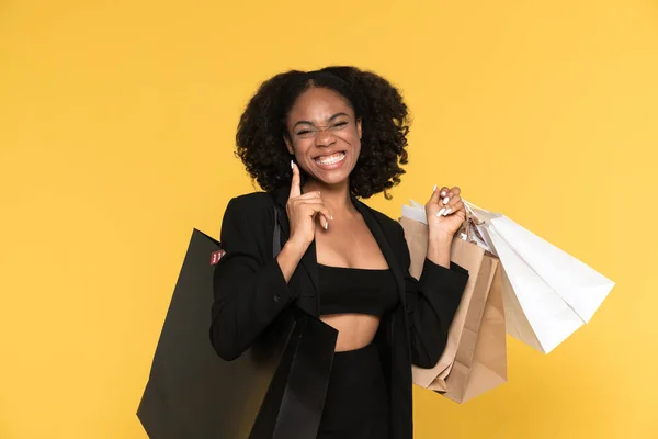 Black woman pointing fingers upward while posing with shopping bags isolated over yellow background
