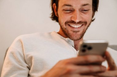 Kızıl saçlı adam evdeki kanepede dinlenirken cep telefonu kullanıyor.