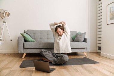 Kızıl adam evde yoga yaparken dizüstü bilgisayar kullanıyor.