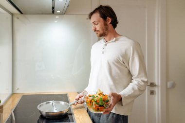 Kızıl saçlı adam evde sebzelerle yemek yapıyor.