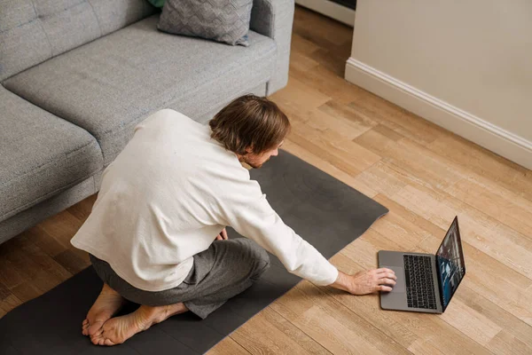 Ginger man using laptop during yoga practice on floor at home