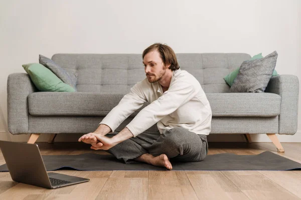 Ginger man using laptop during yoga practice on floor at home