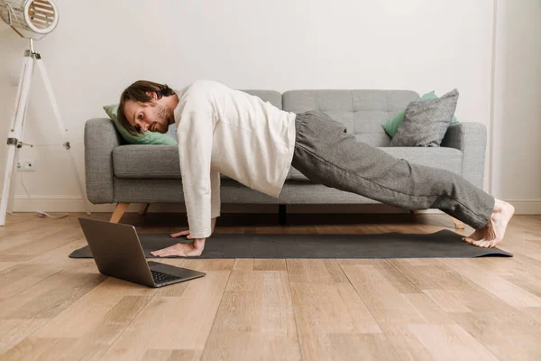 Ginger man using laptop during yoga practice on floor at home