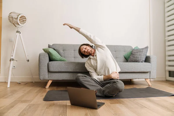 Ginger man using laptop during yoga practice on floor at home