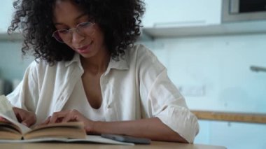 Pretty curly haired woman in eyeglasses reading book in the morning at home