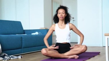 Pretty curly haired woman doing breathing exercise on the yoga mat at home