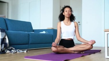 Confident curly haired woman doing meditation on the yoga mat at home