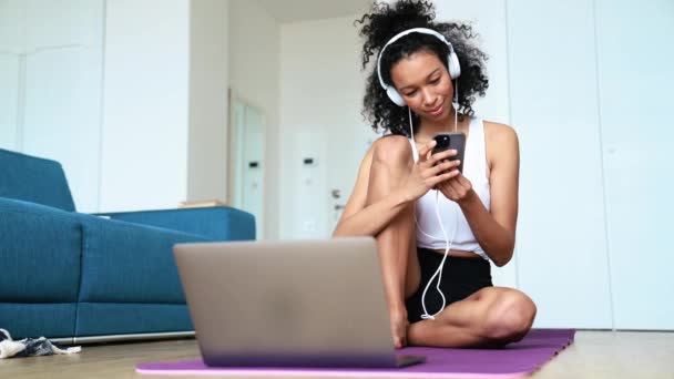 Smiling Curly Haired Woman Typing Phone Headphones Yoga Mat Home — Stockvideo