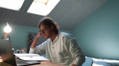 Positive blond man wearing eyeglasses reading book at home indoors