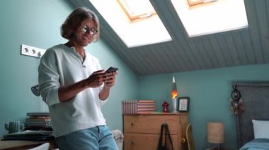 Happy blond man typing on smartphone at home indoors