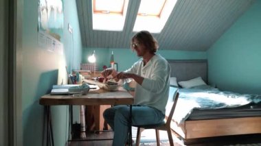 Smiling blond man wearing eyeglasses eating food at home indoors