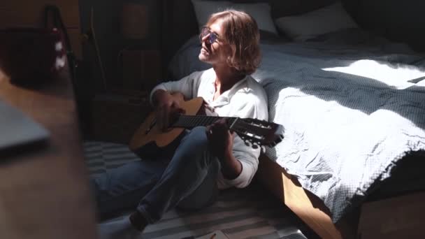 Pretty Blond Man Wearing Eyeglasses Playing Guitar Sitting Floor Home — Vídeos de Stock