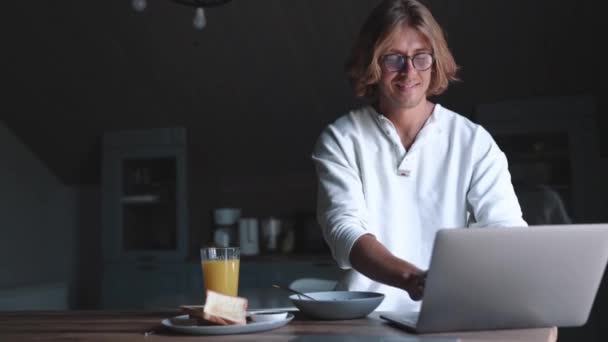 Handsome Blond Man Wearing Eyeglasses Typing Laptop Eating Breakfast Home — 图库视频影像