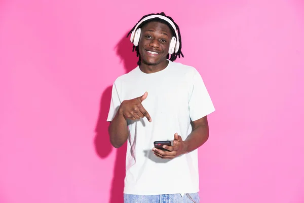 Black Man Listening Music While Pointing Finger Cellphone Isolated Pink — стоковое фото