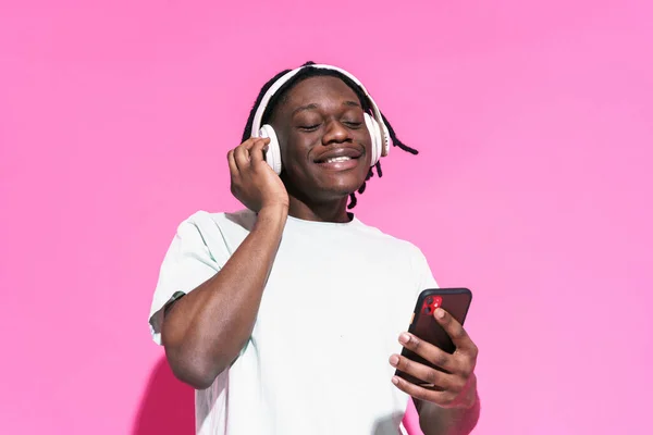 Young Black Man Listening Music Using Mobile Phone Isolated Pink — стоковое фото