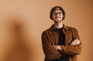 Tıraşsız, gözlüklü, gülümseyen ve bej arka planda izole edilmiş kameraya bakan beyaz bir adam.