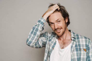 Tıraşsız beyaz bir adam gülümsüyor ve gri arka planda izole edilmiş kameraya bakıyor.