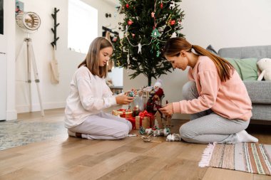 White mother and daughter decorating christmas tree together at home
