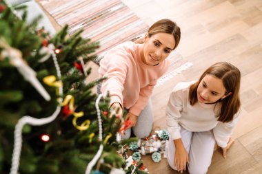 White mother and daughter decorating christmas tree together at home