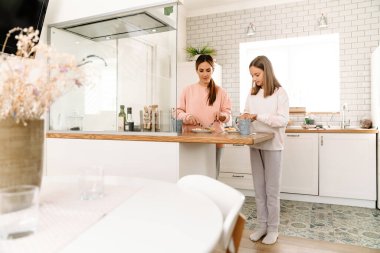 White mother and daughter having breakfast together in kitchen at home