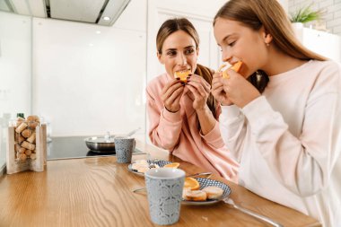 White mother and daughter having breakfast together in kitchen at home