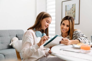 White girl doing homework with her mother while having breakfast at home