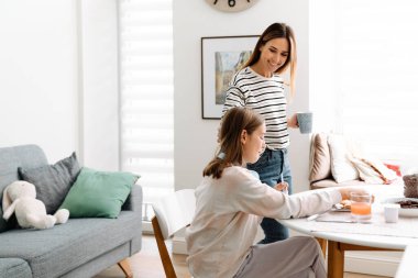 White mother and daughter smiling while having breakfast at home