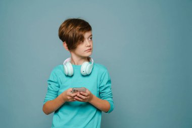 Ginger white boy with headphones using mobile phone isolated over blue wall
