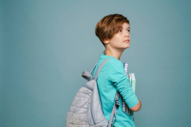 Ginger white boy posing with exercise books and backpack isolated over blue wall