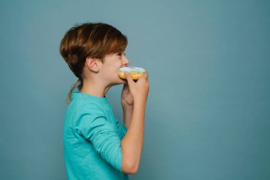 Ginger white boy wearing long sleeve eating doughnut isolated over blue wall
