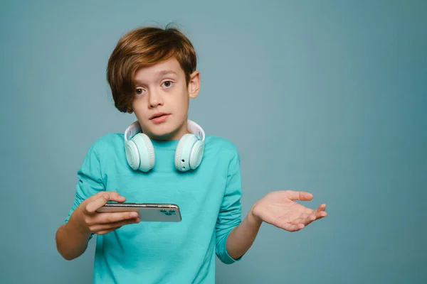 Perplexed Boy Gesturing While Playing Online Game Cellphone Isolated Blue — ストック写真