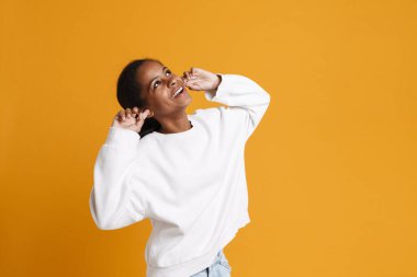 Brunette black girl laughing while plugging her ears isolated over yellow background