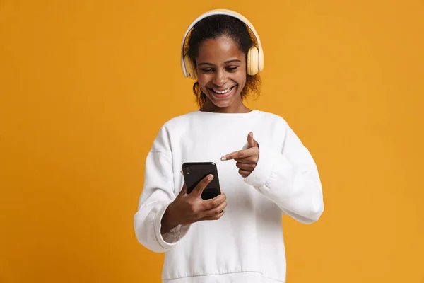 Brunette Black Girl Headphones Pointing Finger Her Cellphone Isolated Yellow — Fotografia de Stock