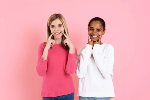 Багаторасові Дві Дівчини Светрах Вказують Пальці Посмішки Ізольовані Над Рожевою — стокове фото