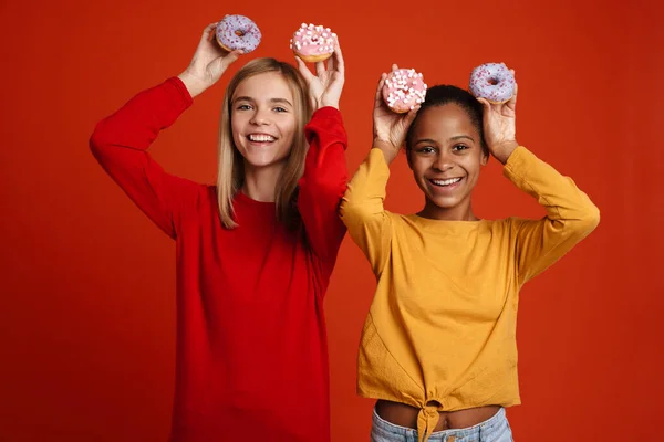 Multiracial Two Girls Laughing While Making Fun Donuts Isolated Red — стоковое фото
