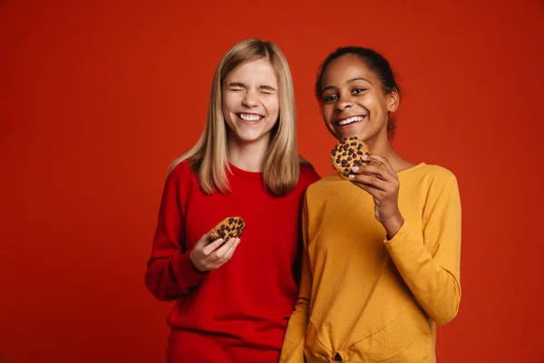 Multiracial Two Girls Laughing While Posing Cookies Isolated Red Wall — 스톡 사진