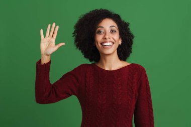 Black young woman smiling and waving hand at camera isolated over green background