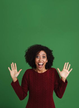Black excited woman wearing sweater screaming while gesturing isolated over green background