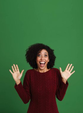 Black excited woman wearing sweater screaming while gesturing isolated over green background