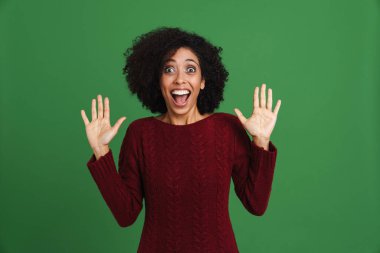Black excited woman wearing sweater screaming while gesturing isolated over green background