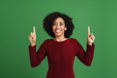 Black young woman wearing sweater pointing fingers upward isolated over green background