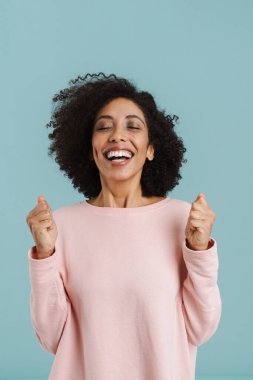 Young black woman laughing while posing with clenched fists isolated over blue background