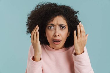 Young black woman with curly hair expressing surprise at camera isolated over blue background