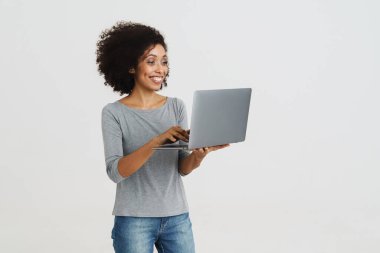 Young black woman with curly hair smiling and using laptop isolated over white background