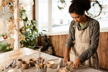 Young black ceramist woman wearing apron sculpting in clay at her workshop