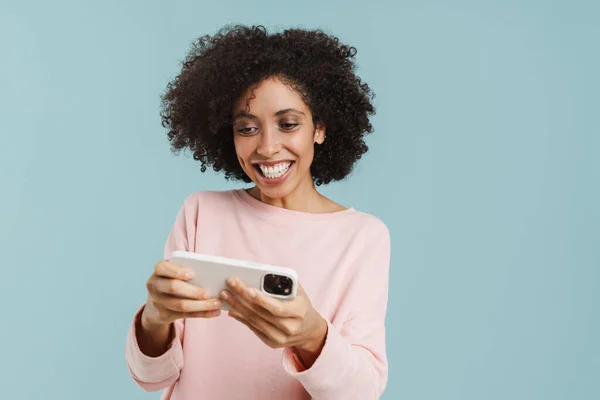 Young Black Woman Smiling Playing Online Game Cellphone Isolated Blue — ストック写真
