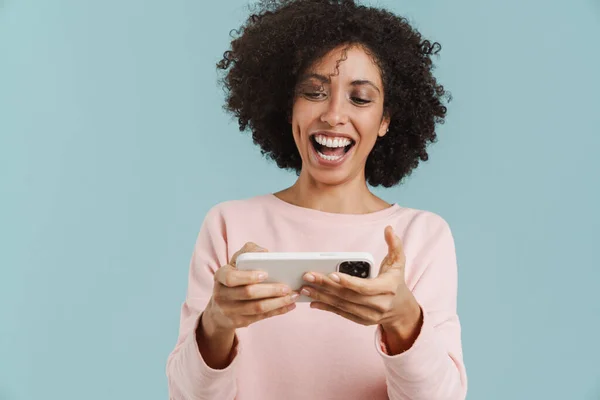 Young Black Woman Laughing Playing Online Game Cellphone Isolated Blue — стоковое фото