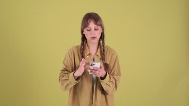 Smiling blonde woman with pigtails talking by video call on mobile in the green studio
